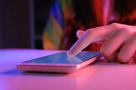 Use of mobile phone in trendy neon lights. Creative vivid color of ultraviolet red and blue. Hands of Teen Girl scrolling up photos Close-up at dark neon room. App for sale in shop. social media.の写真素材