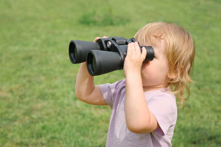 Little girl using binoculars in a forest. 2 years kid looking ahead. Smiling baby with spyglass. Adventure, Imagination, travel concept. Freedom vacation. Happy child playing outdoor in summer fieldの写真素材