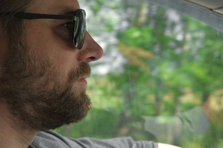Confident Bearded man in a sunglasses driving a car during jorney trip. Side view from passenger...