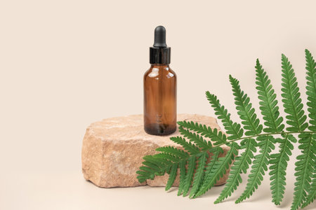 Dark amber glass bottle standing on stone. Natural skin care SPA beauty product design. Mineral organic oil cosmetics. Beige background. mock up. Oily pipette. face and body treatment. front view standの写真素材