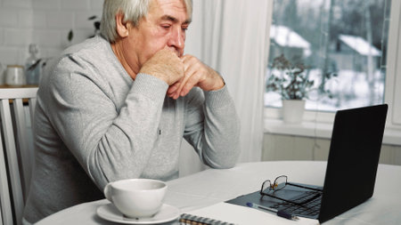 Old man Thinking at laptop. Pensive Mature Gray hair 60s - 70s Aged Man Sitting at Table with...