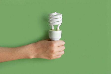 Compact fluorescent lamp Lamp in human hand. Helical integrated CFL Lightbulb on green pastel color background. Idea, creativity concept. Flat lay design. Banner, top view photo. mockup. Lighting, ecoの写真素材