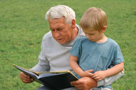 Happy grandfather reading book to curious grandson outdoors. close up. Grandpa with grandchild...