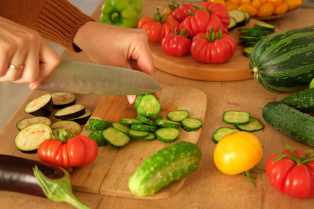 Woman using a knife cutting fresh raw vegetables. Tomatoes, cucumbers being sliced on a wooden...