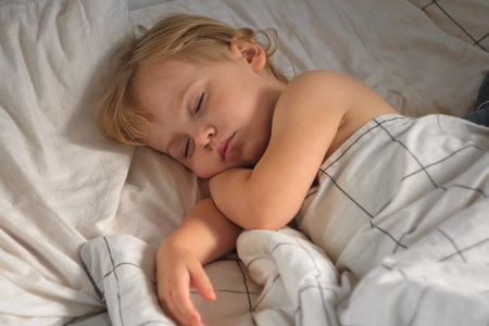 Peaceful adorable baby sleeping on a bed at home. Slumbering little child. Two year old girl sleeps peacefully at domestic room interior background. Serene dream. cute face close up. deep kid slumberの写真素材