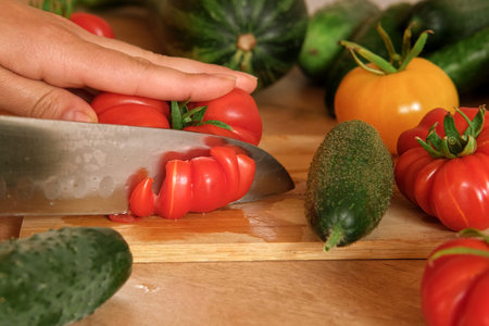 Woman using a knife cutting fresh raw vegetables. Tomatoes, cucumbers being sliced on a wooden board. Cooker at home making a healthy veggie meal. Chopping ingredients for preparing vegetarian dish 4Kの写真素材