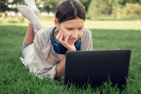 Teenage schoolgirl studying reading her books, tablet and notebook, sitting outdoors. back to...