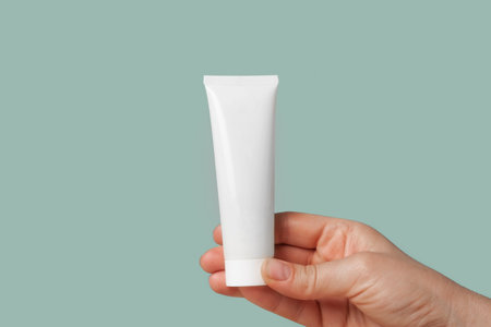 White Cream Package Template in Female Hand. Green Background. Natural Cosmetics Showing. Beauty Product Mockup. Skincare, Facial mask, Toner. Front View Soft Shadow. Trendy Bottle. Spa Anti-agingの写真素材