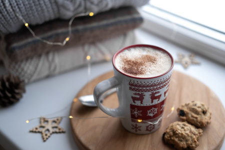 Winter windowsill still life. Red ceramic cup of hot coffee on window sill. Christmas decorations on...