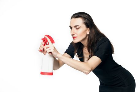 The fatal woman in a black dress with a spray for washing glasses squinted and tries to scrape...