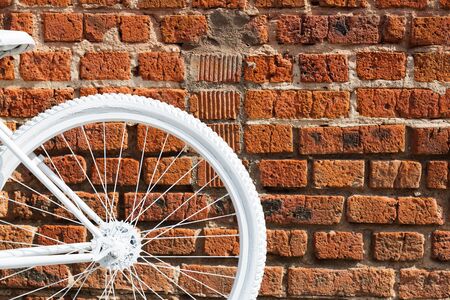 White painted decorative wheel of an old bicycle with a basket of flowers against a brick wall.の写真素材