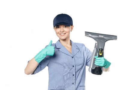 Young white woman in a maid uniform and a baseball cap holds a steamer in her hands and smiles...
