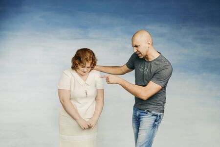 A tall bald man and plump red-haired attractive woman on a blue background, the husband scolds his wife and screams at her with a wave of his handの写真素材