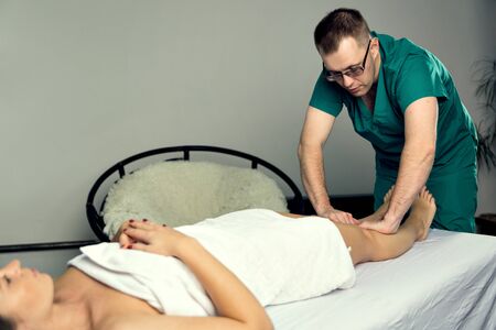 A male massage therapist massages the feet and legs of female legs.