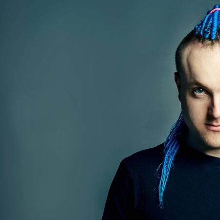 portrait of a young man with an unusual hairstyle of mohawk from blue braids in sportswear posing...