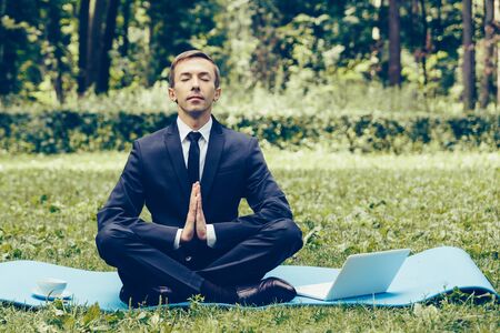 Man in a suit with tie. Business man relaxing in a park in the lotus position, he can't relax in any way, meditation in the park.の写真素材