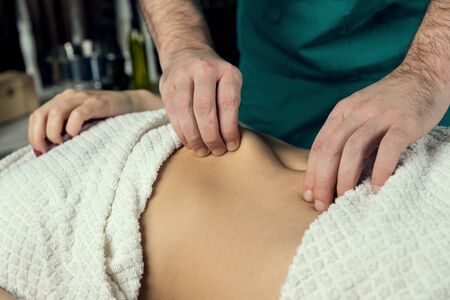 Hands of a masseur's man doing a massage of the abdomen. Close upの写真素材