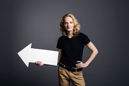 A handsome young guy with long blonde hair and a smile face holds a white arrow pointing to the...