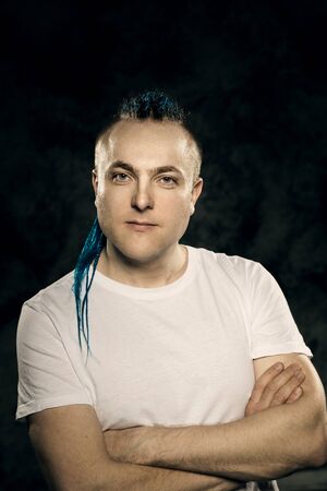 Portrait of a young man with an unusual hairstyle of mohawk from blue braids in sportswear posing...