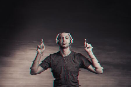 Cool bald man in a gray T-shirt and jeans jumping and fooling around and dancing in headphones with virtual glitch effect.の写真素材