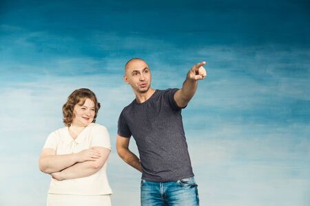 A plump red-haired attractive woman and a tall bald man on a blue background, look to the side, he...