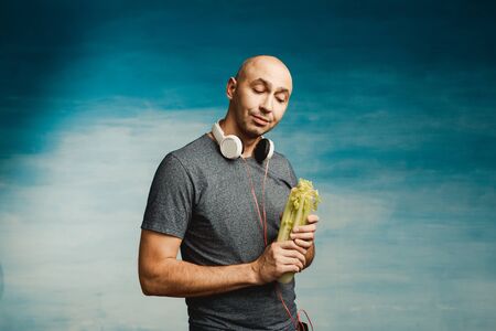 Funny bald man in headphones on his neck lustfully looks at the celery in his hands