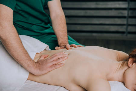 The hands of a male masseur doing massage of a young woman. Beautiful relaxed face of a young womanの写真素材