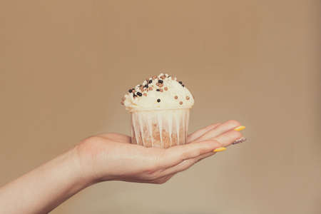 cupcake with white cream decorated with balls of confectionery powder in the hands of a woman.の写真素材