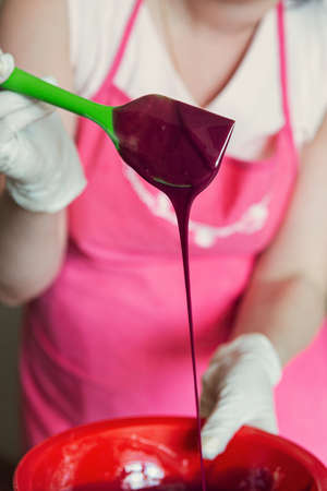 The process of making burgundy frosting for a mousse cake. The girl mixes the icing in a plate with a spatula.の写真素材