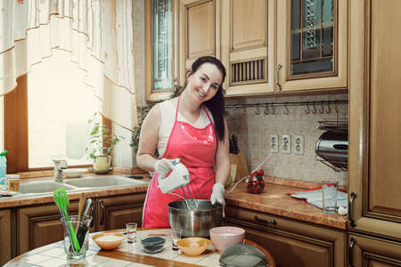 Brunette woman prepares with a mixer Chocolate butter cream in a metal bowl. Beating cream cake. Mixer whisk in creamの写真素材