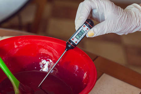 The process of measuring the temperature of pink icing for a mousse cake using a special thermometer.の写真素材