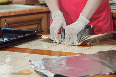 Young woman preparing baking dish for pouring dough. foil wrapping.