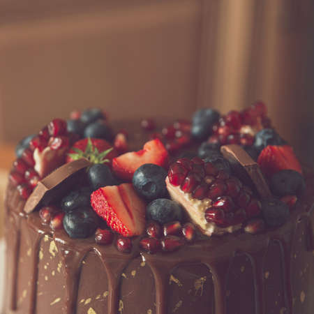 Appetizing chocolate cake decorated with strawberries, blueberries and a pomegranate on an orange background.の写真素材