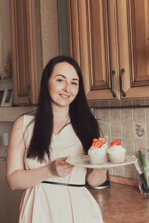 Brunette girl in pink dress holds cupcakes with white cream decorated with strawberries