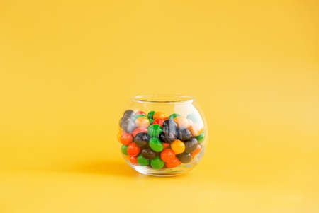 A round jar with multi-colored sweets on a yellow background.の写真素材