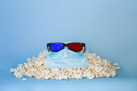 A slide of popcorn, 3D glasses and a medical mask on a blue backgroundの写真素材
