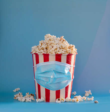 A bucket with a medical mask on it full of popcorn with a slide on a blue backgroundの写真素材