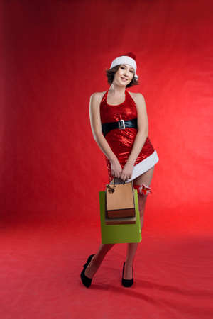A young woman elf dressed as Santa in round glasses holds d background, hands holding a gift package, many paper bags from the store.の写真素材
