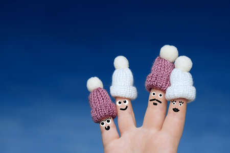Female palm on a blue background, four fingers with painted eyes dressed in funny tiny knitted hats....