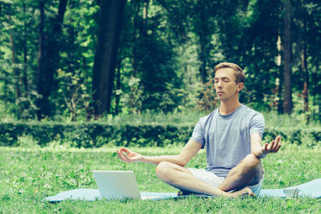 Young attractive man in sport clothes is meditating in the lotus position with a pacified faceの写真素材