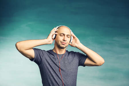A bald man listens music in large headphones, Looks in surprise at the camera on a blue backgroundの写真素材