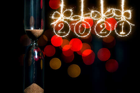 Christmas balls made of sparklers and the inscription 2021. gainst the background of an hourglass...