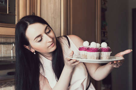 Cupcakes with violet cream decorated with balls topped with coconut crumbs in the hands of a woman in a pink dressの写真素材