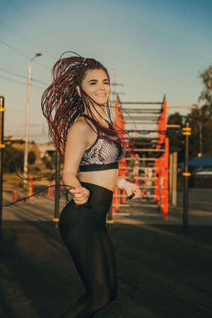Young attractive woman with braided hairstyle jumping rope on the city sports ground.