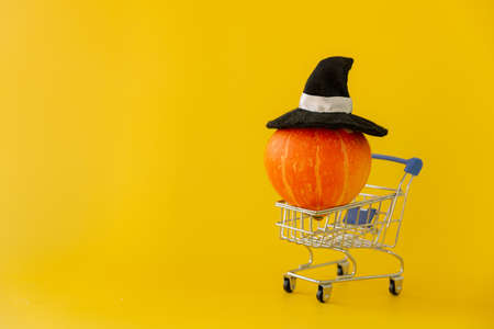 Pumpkin in a witch hat for Halloween in a shopping cart on a yellow backgroundの写真素材