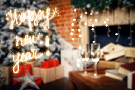 Happy New Year lettering with sparklers on background two glasses with champagne on the table against of New Year decorations and a Christmas tree.の写真素材