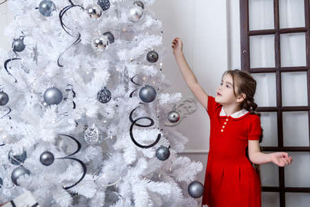 Little girl decorates the Christmas tree in red dress.の写真素材