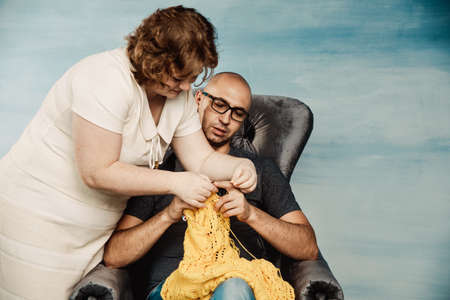 A bald man with a funny face and glasses obliquely knits while sitting on a wreck. Come on skillful...