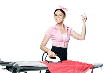 Snaps fingers. A beautiful girl dressed in pin-up style is ironing clothes looks at the camera and smiles isolated on a white background.の写真素材