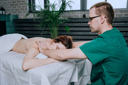Massage therapist doing shoulder massager of a young woman. Beautiful relaxed face of a young woman...
